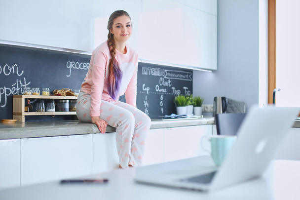 Young woman sitting on table in the kitchen - Foto, afbeelding
