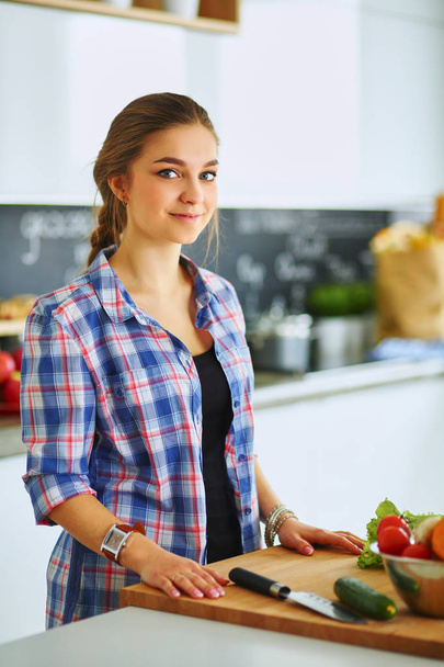 Young woman cutting vegetables in kitchen near desk - Foto, immagini