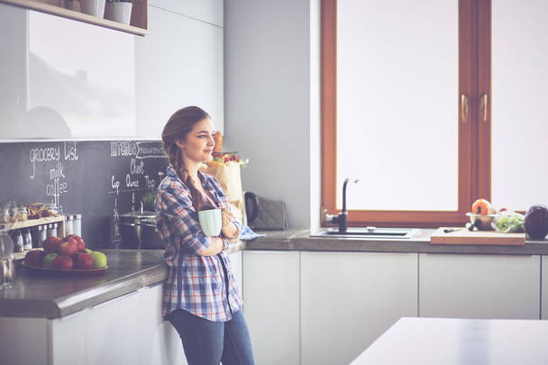 Happy woman drinking tea in the kitchen at home - 写真・画像