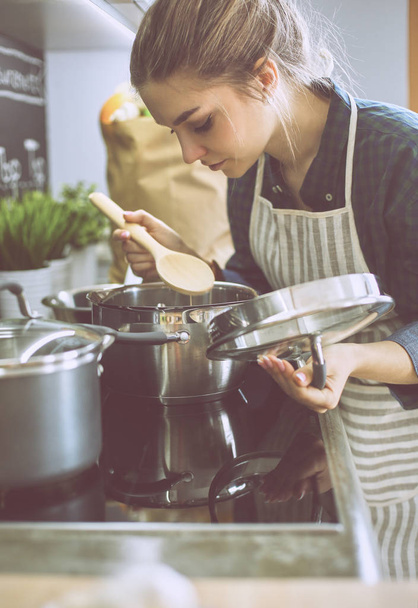 Young woman cooking in her kitchen standing near stove - Foto, imagen