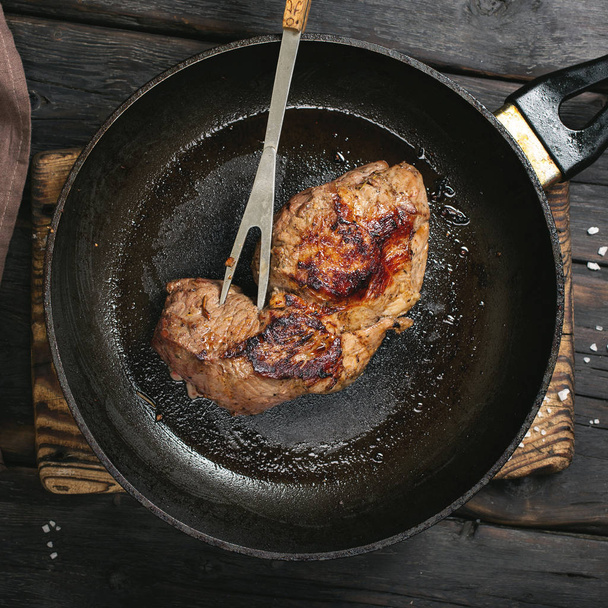 Beef steak in a pan on a dark wooden table - Fotoğraf, Görsel