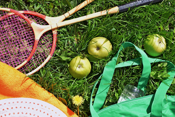 Badminton, hoed, handdoek, rackets en appels op het groene gras. - Foto, afbeelding
