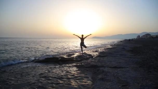 Nuori nainen harjoittelee joogaa rannalla auringonlaskun aikaan. - Materiaali, video