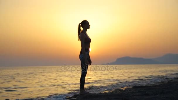 νεαρή γυναίκα σιλουέτα πρακτική της γιόγκα στην παραλία στο ηλιοβασίλεμα. - Πλάνα, βίντεο
