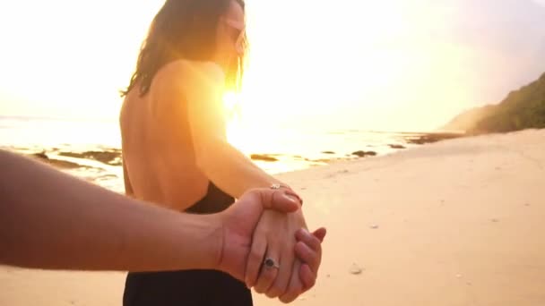 Mladý pár se drží ruce žena předních milenců chůze směrem k západu slunce na prázdné pláži. cestovní koncept - Záběry, video
