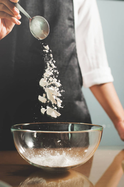 Woman chief sprinkling flour into glass bowl. - 写真・画像