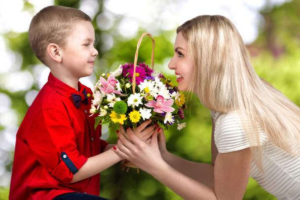 Young beautiful mother with her son.A woman and a baby boy with a bouquet,a basket of flowers.        Spring concept of family vacation. Women's day. - Foto, afbeelding