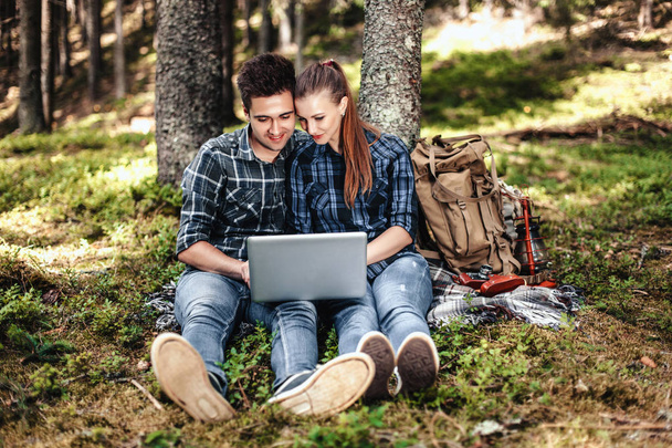 A couple of tourists sitting and looking at laptop in the woods. The concept of active rest - Foto, afbeelding