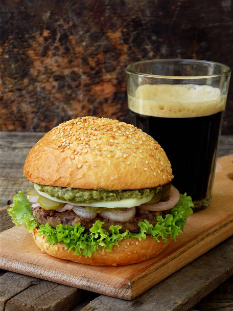 veggie burgers with a chop of black beans, lettuce, pickled onions, cucumber and a glass of dark beer on a wooden background. Space for text - Photo, Image