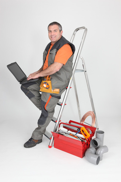 Plumber sitting on stepladder with computer - Foto, immagini