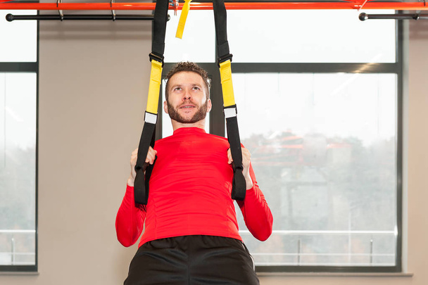 Sporty male exercising do y deltoid fly with fitness trx straps in gym - Foto, afbeelding