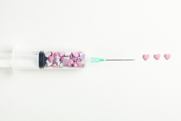 Syringe filled with heart shaped candy on a white background - Fotoğraf, Görsel