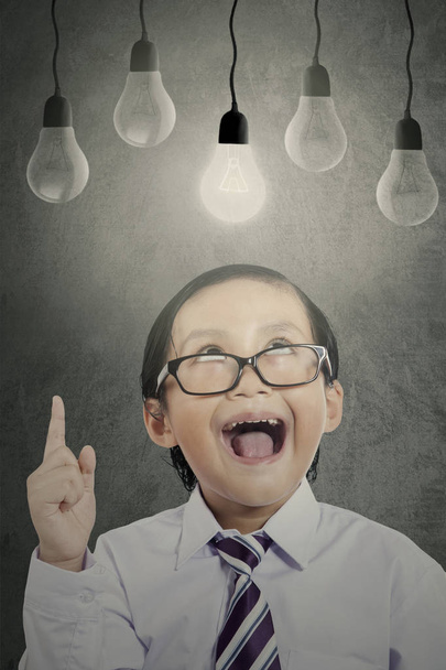 Cheerful boy with bright bulb on classroom - Foto, afbeelding
