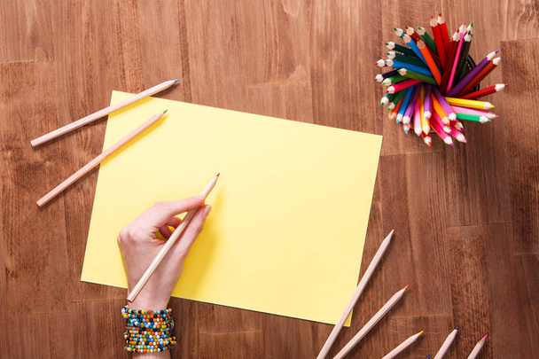 Tyttö käsi piirustus, tyhjä keltainen paperi ja värikkäitä kyniä puinen pöytä
 - Valokuva, kuva