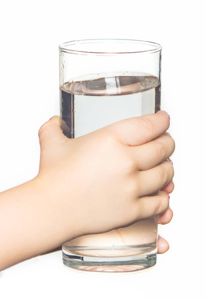 the child holds a glass of water in his hands. selective focus.  - Фото, изображение