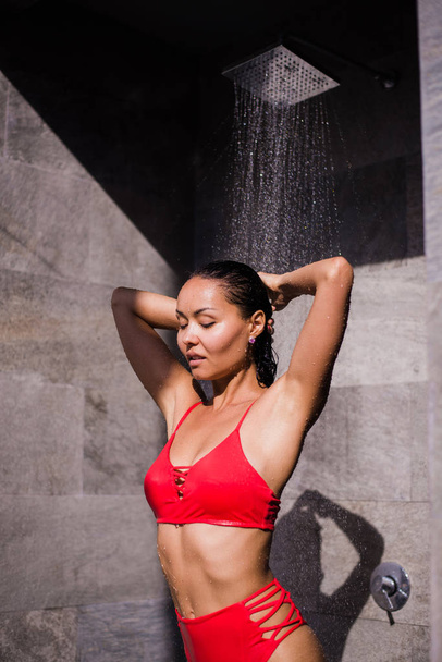 eine junge sexy Frau im roten Badeanzug duscht draußen im Luxushotel - Foto, Bild