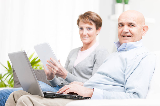 Пара середнього віку розслабляється з мобільними пристроями
 - Фото, зображення