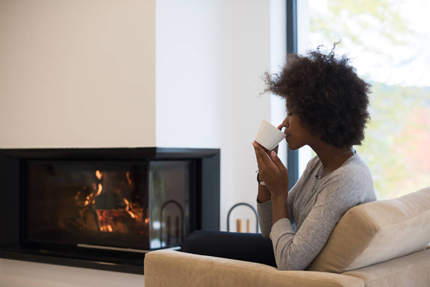 black woman drinking coffee in front of fireplace - Fotoğraf, Görsel