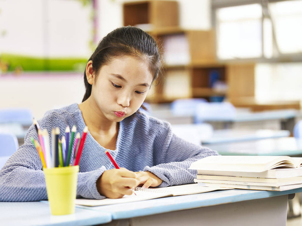 ázsiai elemi iskolás csinál házi feladatot osztályteremben - Fotó, kép