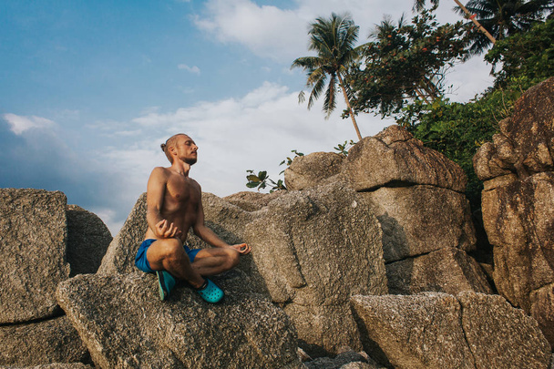 Człowiek w rock w pozycji lotosu. Mężczyzna siedzący na ogromny kamień - Zdjęcie, obraz