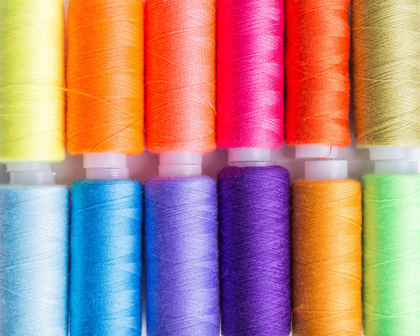 Sewing threads of different colors stacked side by side on a wooden surface. - Photo, Image