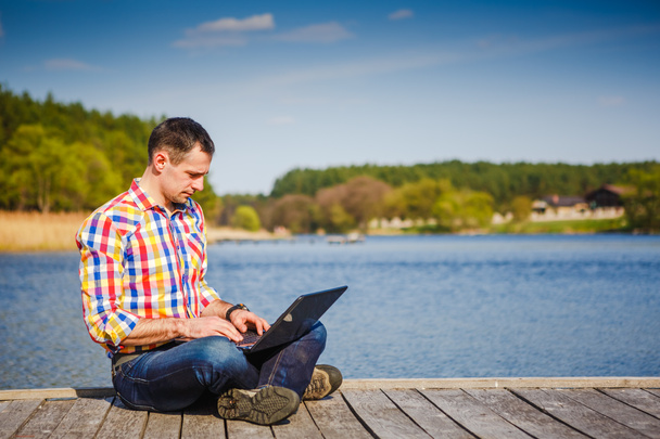 Jeune homme avec ordinateur portable travaillant en plein air
 - Photo, image