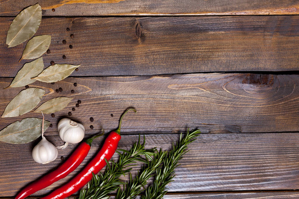 Chile rojo y ramitas de romero con hojas de laurel y cabezas de ajo blanco sobre fondo de madera
 - Foto, Imagen