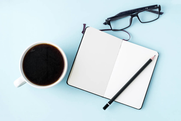 Mesa de oficina azul con bloc de notas en blanco, lápiz, vasos y taza de café blanco. Copia espacio para texto. Acostado. Vista superior
. - Foto, Imagen