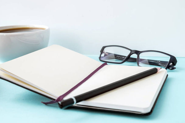 Office blue table with blank notepad, pencil, glasses and coffee cup. Copy space for text. - Zdjęcie, obraz