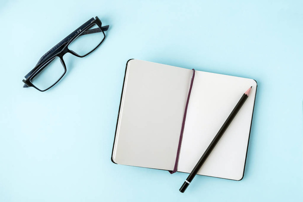 Office blue table with blank notepad, pencil, glasses. Copy space for text. Flat lay. Top view. - Photo, Image