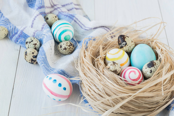 Colorful Easter Eggs on the white rustic wooden background with nest and linen towel. Selective focus. - Foto, immagini