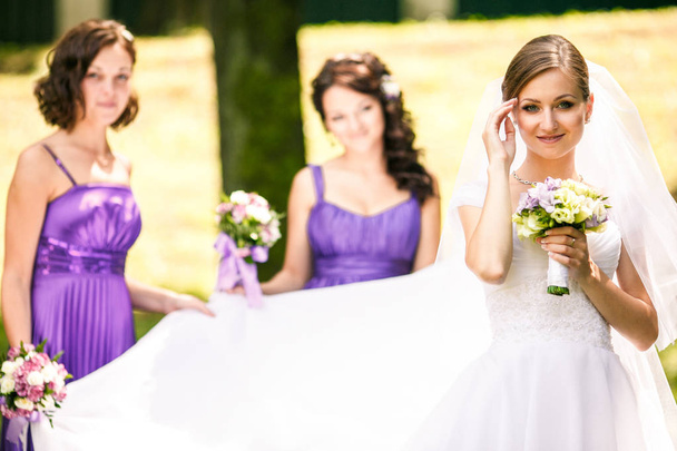Bride looks pretty in her dress while bridesmaids stand on the b - Photo, Image