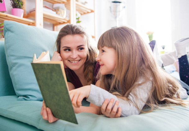 Mother and daughter sitting on sofa and reading book together - Φωτογραφία, εικόνα