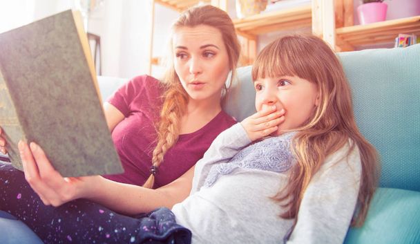 Mother and daughter sitting on sofa and reading book together - Foto, Imagem
