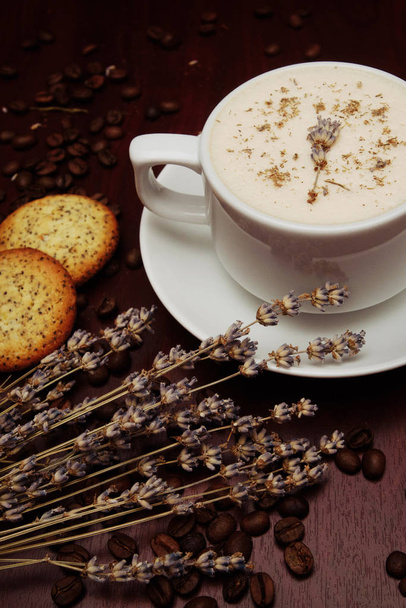 Φλιτζάνι καφέ με γάλα, μουνί-ιτιά και ξερά κλαδιά και φύλλα σε καφέ φόντο. - Φωτογραφία, εικόνα