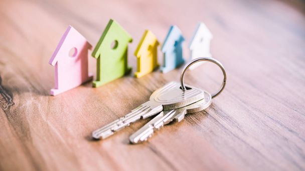 Silver Keychain in front of colourful miniature symbol of houses laying on the wooden surface - 写真・画像