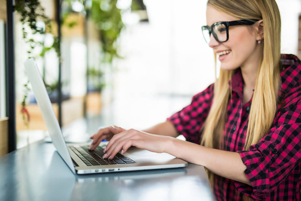 若い女性起業家作業の座っている机のオフィスで彼女のラップトップ コンピューター上で入力側からの眺め - 写真・画像