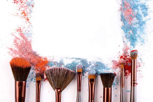 Pinceaux de maquillage avec fard à joues ou fard à paupières de tons rose, bleu et corail saupoudré sur fond blanc
 - Photo, image