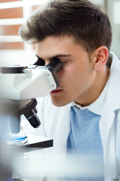 Young man looking through microscope in laboratory. - Фото, изображение