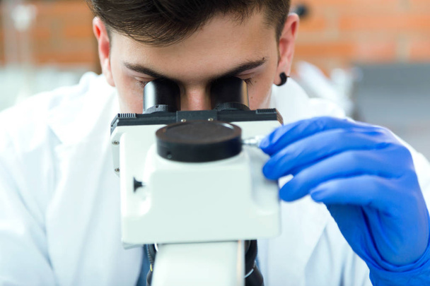 Young man looking through microscope in laboratory. - Foto, Bild