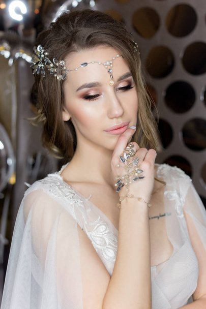 gentle portrait of a beautiful cute happy bride with a beautiful hairdo festive bright make-up in a wedding dress with earrings and a ring with an ornament in her hair - Foto, imagen