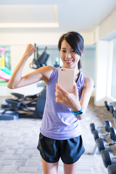 Mujer mostrando músculo y tomando selfie delante del espejo
 - Foto, Imagen