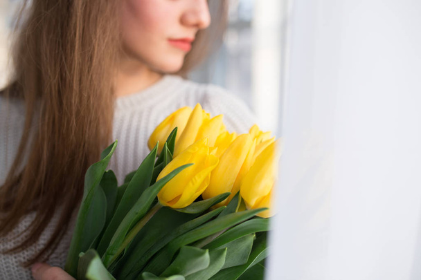 Portrait of beautiful woman holding yellow tulips - cropped photo - 写真・画像