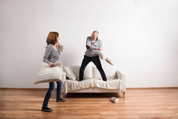 Beautiful senior couple having a pillow fight. Studio shot. - Fotó, kép