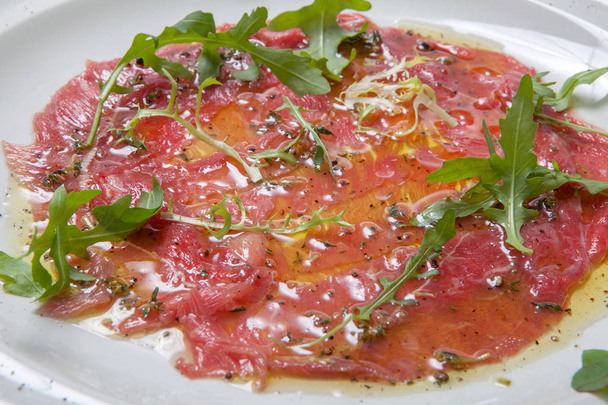 Beef carpaccio garnished with fresh arugula on white plate - 写真・画像