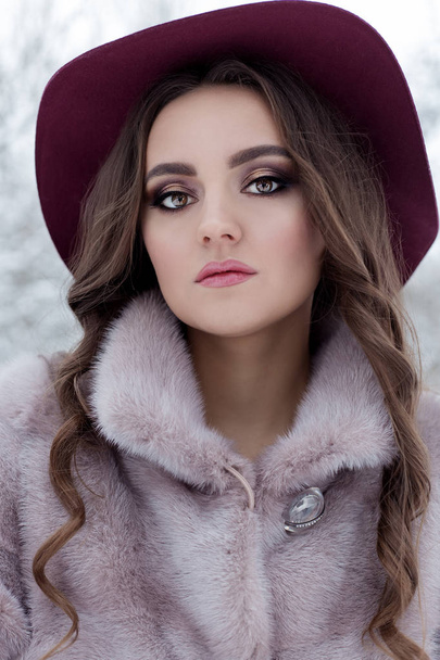 beautiful cute elegant girl in a fur coat and hat walking in the winter forest bright frosty morning - Фото, изображение