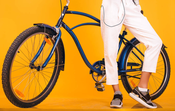 レトロな自転車に合わせて陽気な黄色の背景の前に立っている日、カジュアルな服、ビンテージ自転車に乗って、ストリート ・ ファッションのスタイルを持つ若い女性を発見、感情 - 写真・画像
