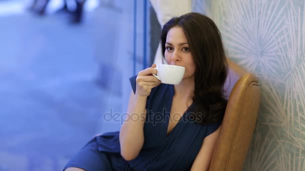 Prores. A young girl in a blue dress is drinking coffee in a cafe - Filmagem, Vídeo