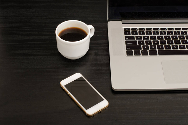 Top view of coffee mug, smartphone and laptop keyboard, black table - 写真・画像