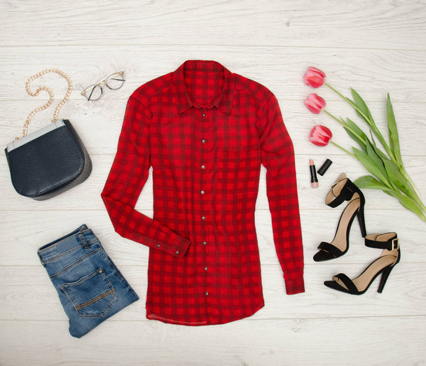 Módní pojem. Červená halenka, džíny, kabelky, sluneční brýle, černé boty, rtěnku a růžové tulipány. Pohled shora, světlé dřevo pozadí - Fotografie, Obrázek